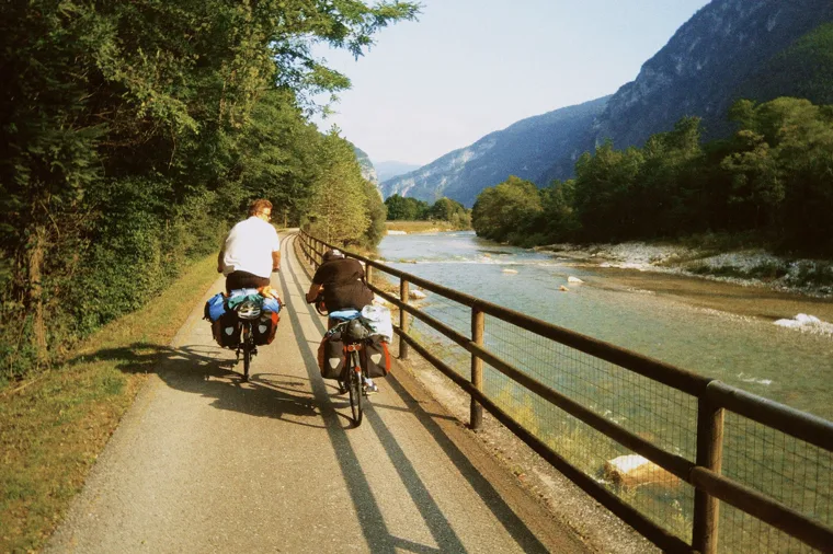 Two loaded touring bikes on a riverside path beside a fast alpine river in warm evening light.