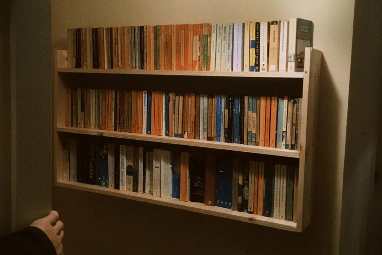 A hand reaching towards a hand-built shelf packed with worn paperbacks.